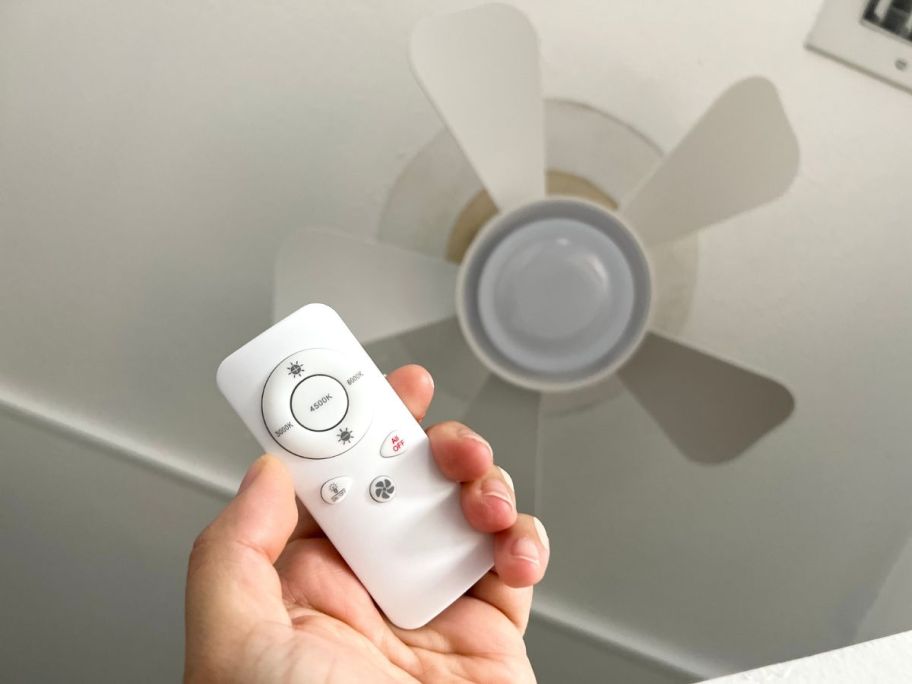 A hand holding a Socket Fan for the ceiling with remote