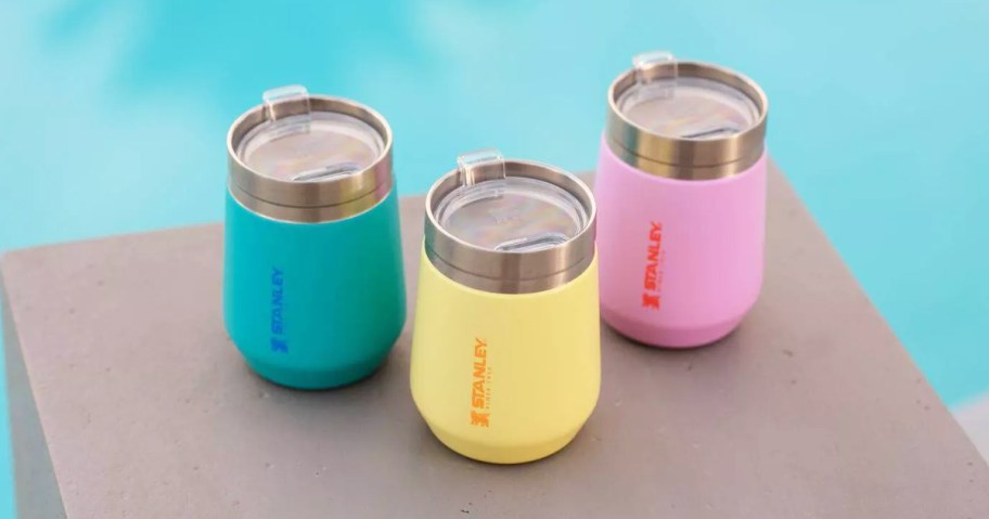 teal, yellow, and pink stanley tumblers near pool