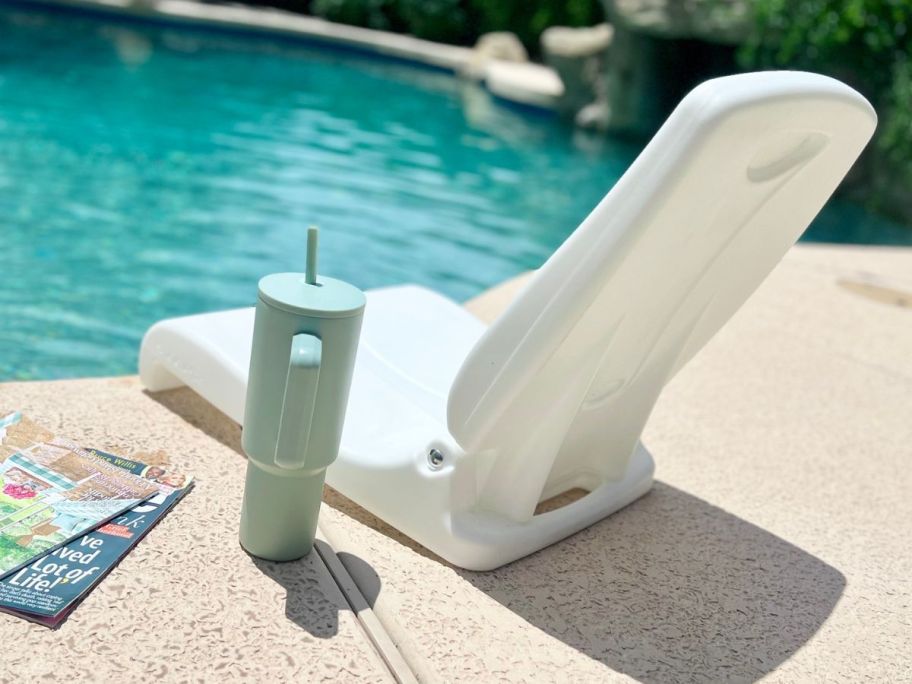 A Step2 Flip seat by the edge of a pool next to a couple of magazines and a tumbler