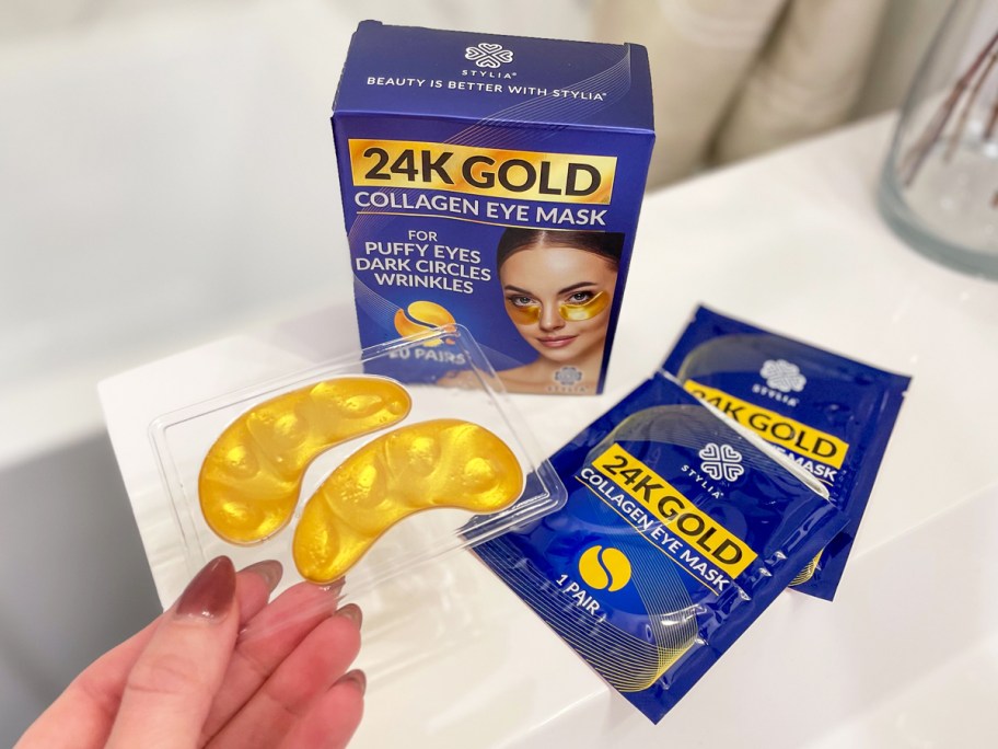 hand holding up a set of gold eye gels with packaging in the background