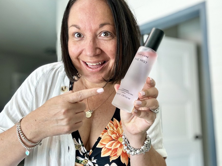 woman holding up and pointing to a bottle of Tan-Luxe Facial Mist