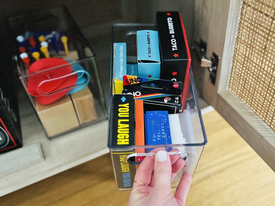 hand grabbing a clear storage container filled with card games