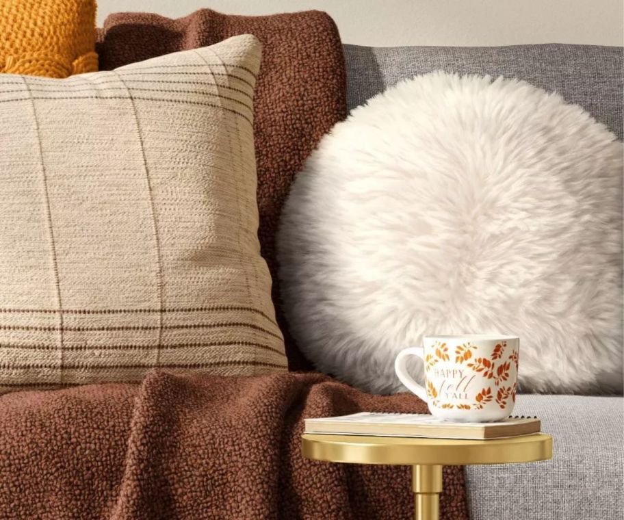 a round faux fur throw pillow on a sofa with other pillows and a throw blanket