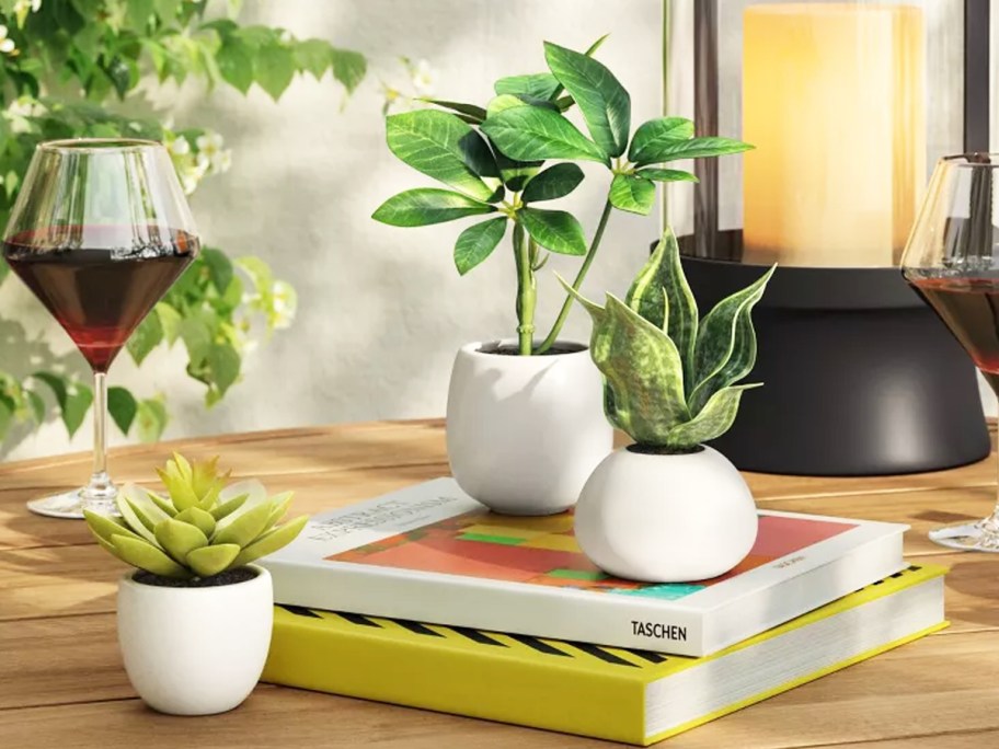 three potted artificial plants on table with books