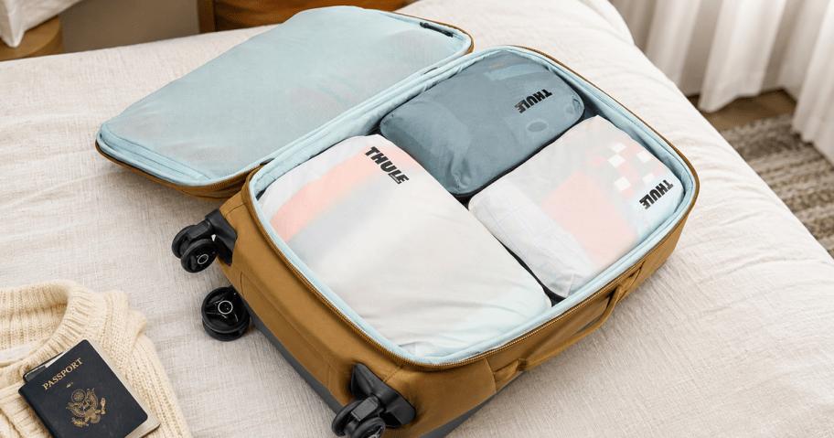 Thule compression packing cubes arranged inside an open suitcase on a hotel bed