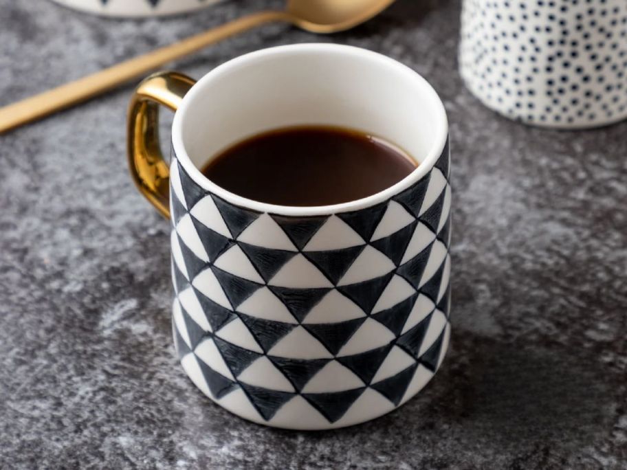 a black and white medallion-patterned coffee mug with a gold handle