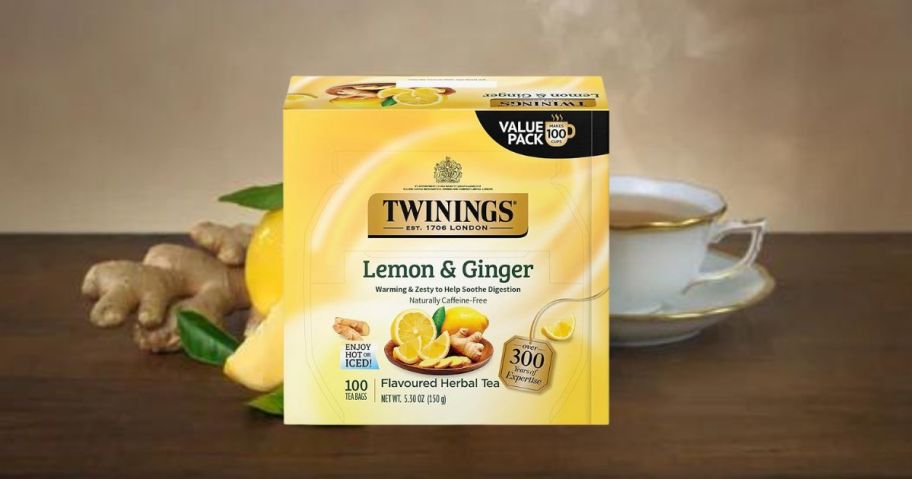 Twinings Lemon & Ginger Herbal Tea box in front of lemons and tea cup on table