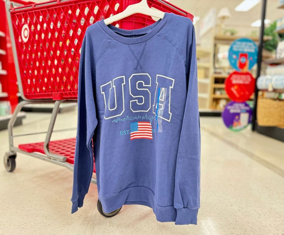 a womens blue USA sweatshirt hanging on the side of a shopping cart in a target store