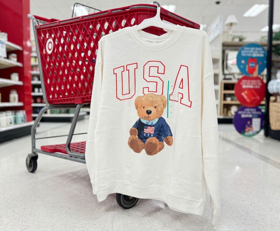 a womens white USA sweatshirt hanging on the side of a shopping cart in a target store