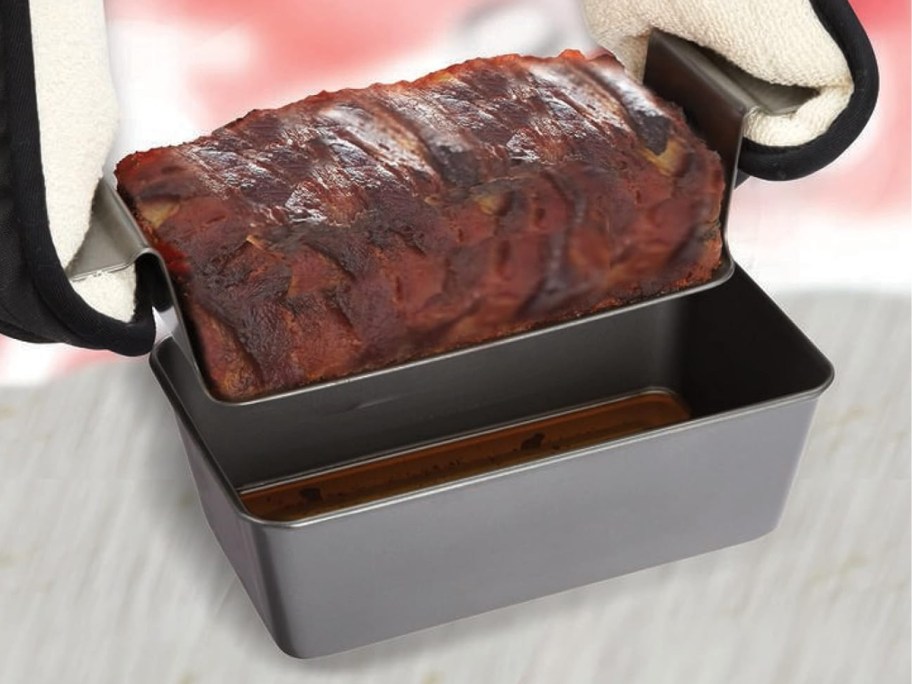 person wearing pot holders lifting a meatloaf out of a loaf pan