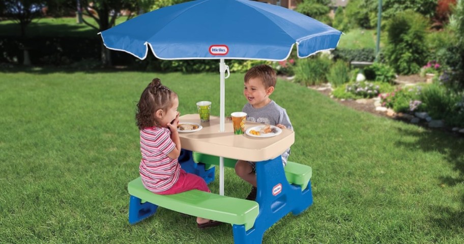 toddler boy and girl sitting at a Little Tikes picnic table with a blue umbrella