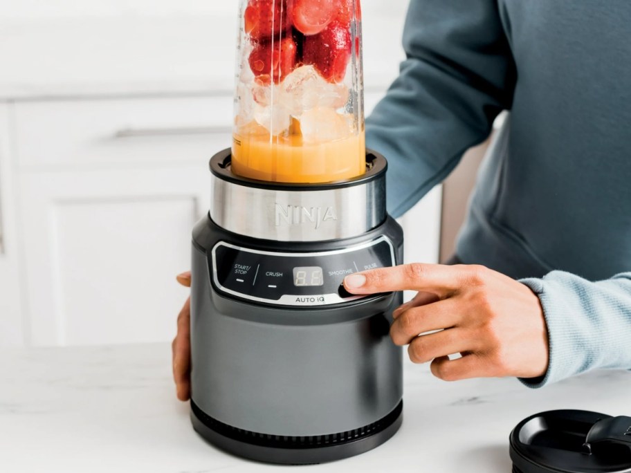 woman pushing a button on a Ninja blender filled with smoothie ingredients