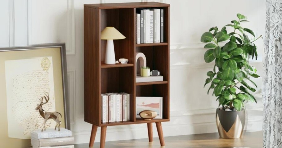 dark brown mid century modern style small bookcase with lighter color legs filled with books and knick knacks