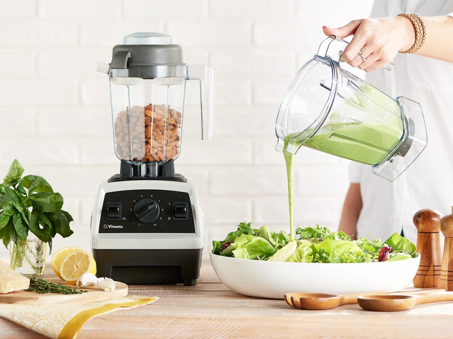 pouring green dressing on a salad next to a vitamix blender