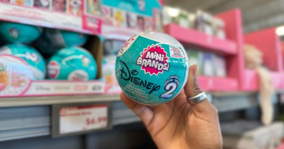 A hand holding a ball of Zuru Mini Brands in a store