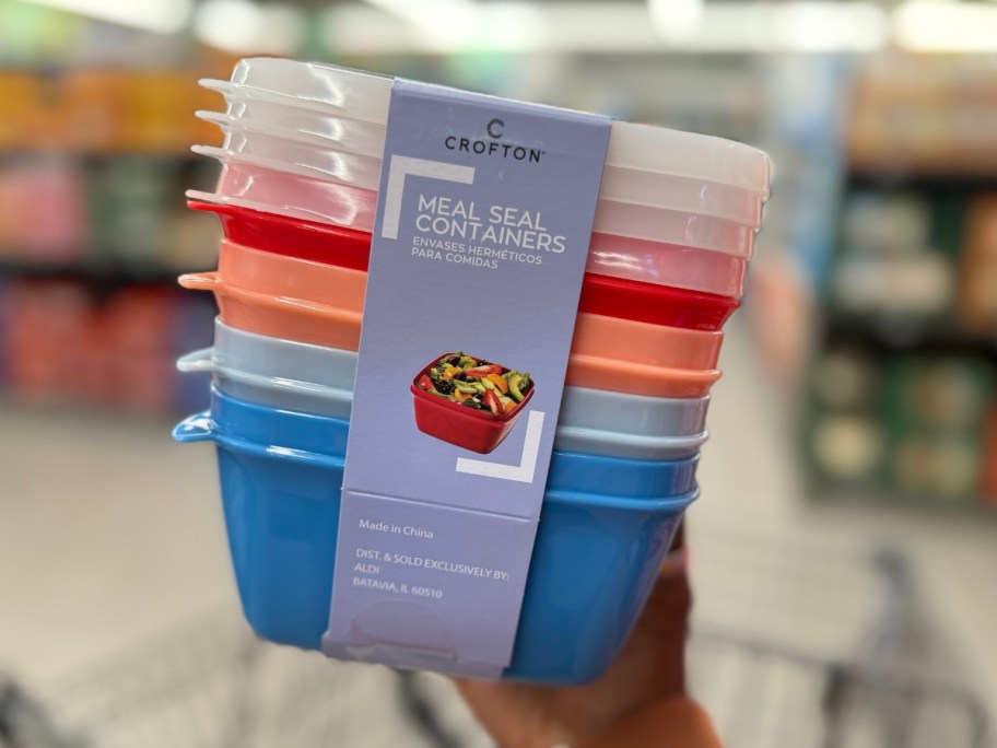 hand holding a pack of 4 colorful food containers with lids in the packaging