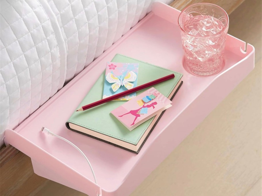 pink bedside table with water cup and green notebook on top