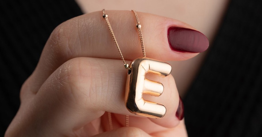 hand holding gold letter E necklace 