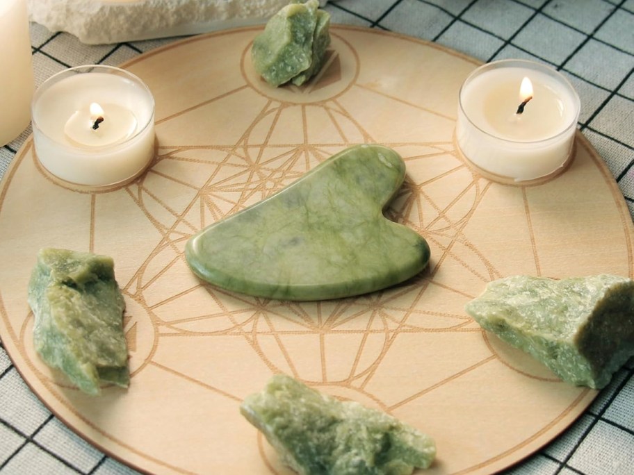 gua sha jade heart on board with candles and rocks