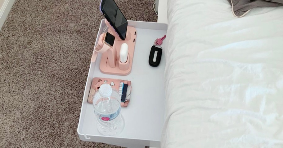 white bedside table on bed with pink phone, watch and water bottle