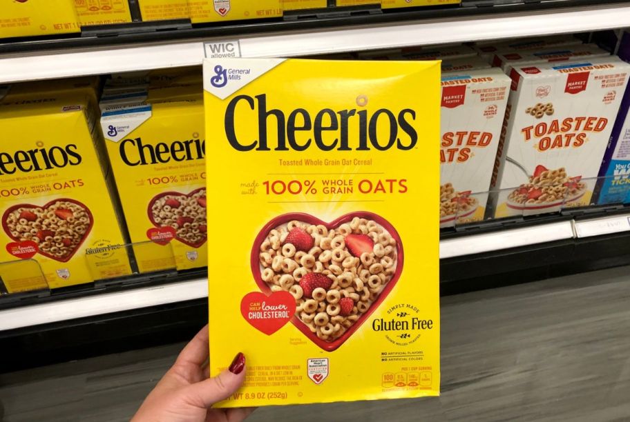 a womans hand holding an 8.9oz box of cheerios