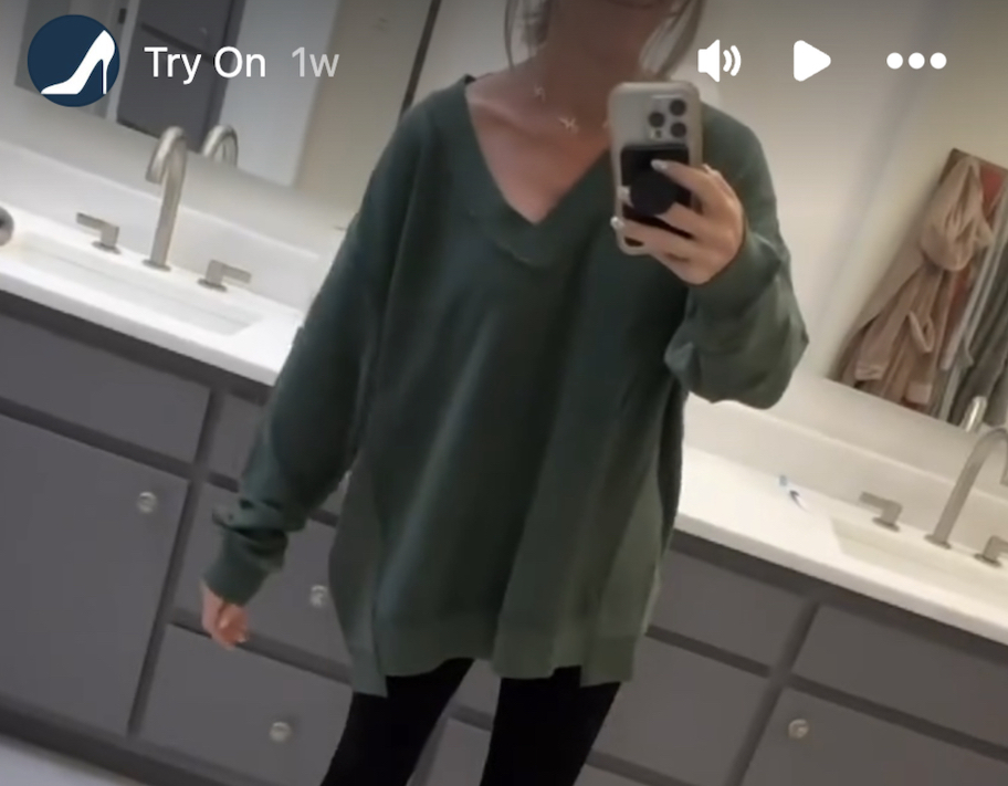 screenshot of woman taking video in mirror of green sweatshirt pullover