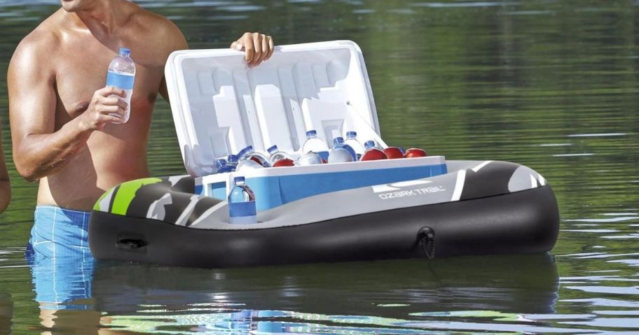 a man standing next to an Ozark Trail Adult Unisex Multicolor Cooler Float floating on the water with a large cooler in it