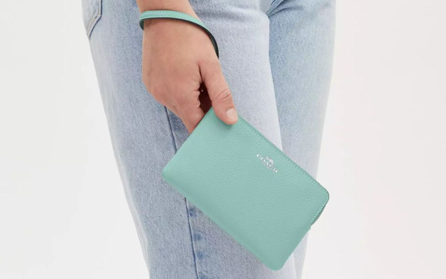 a womans hand holding a coach faded blue corner zip wristlet