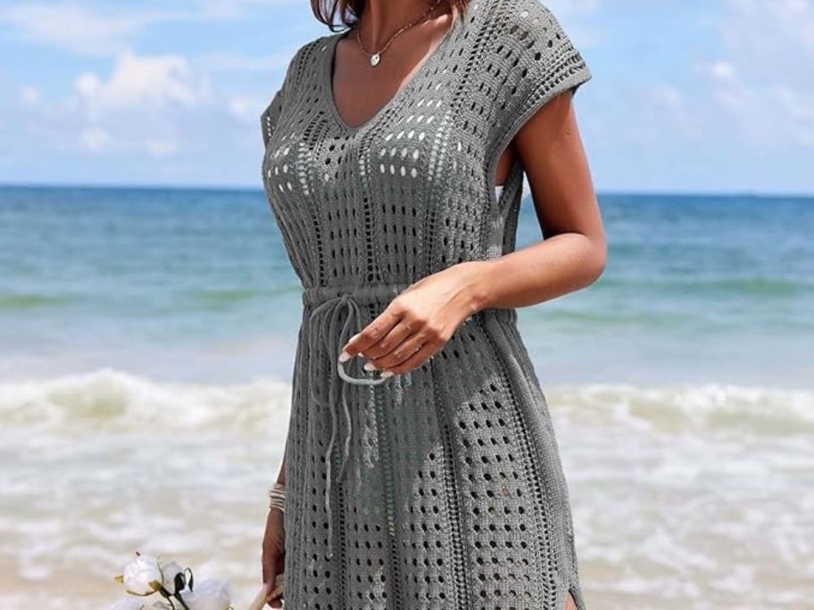 woman wearing AI'MAGE Women's Crochet Cover Up Hollow Out Swimsuit Coverup V Neck Beachwear with Drawstring S-3XL in b-grey on beach