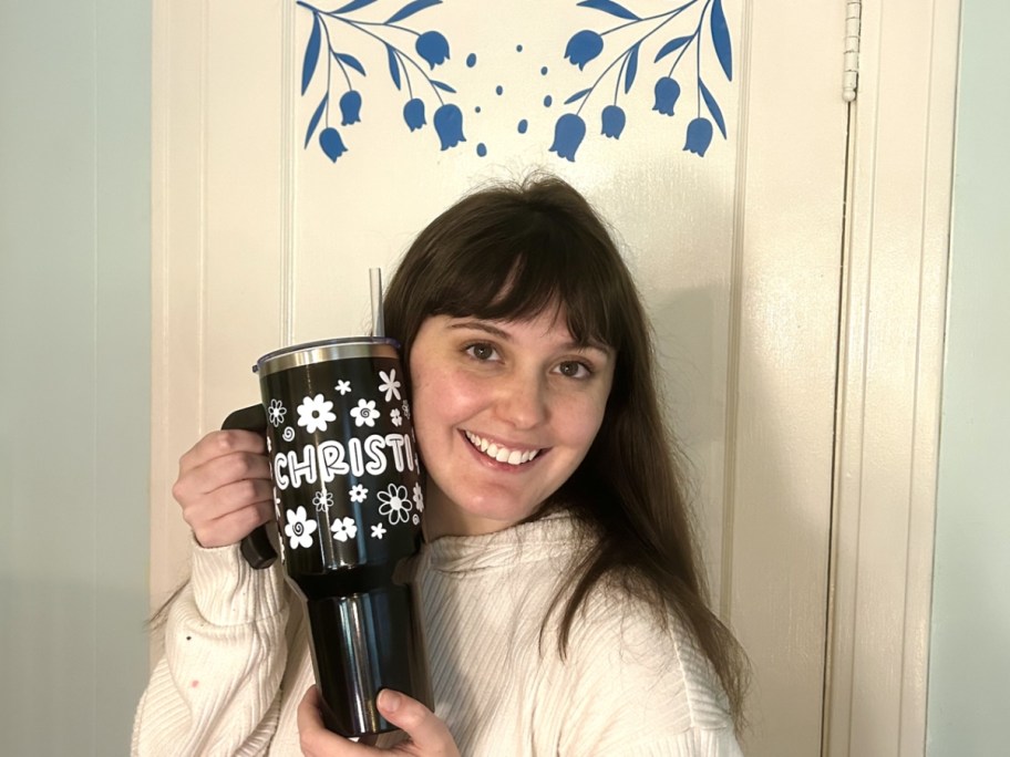 Madison holding up a customized Tumbler, standing in front of a door with custom vinyl decals