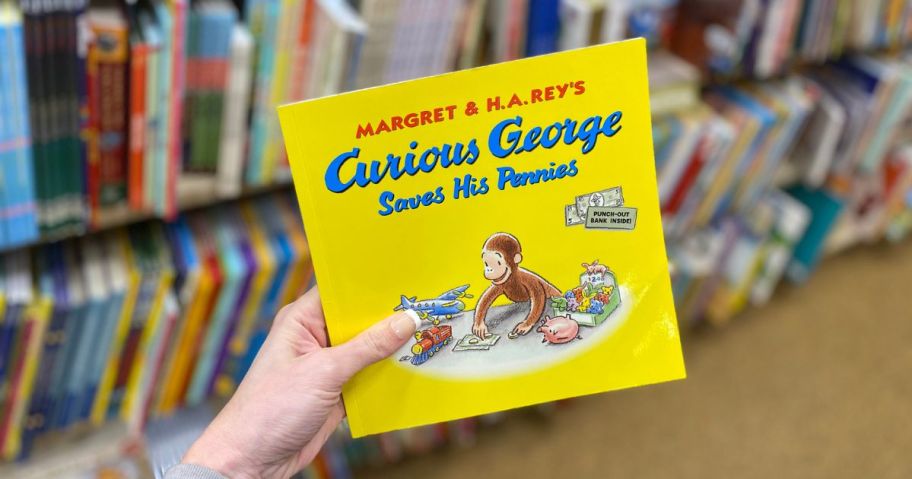 Curious George book being held by hand in store in front of book shelves