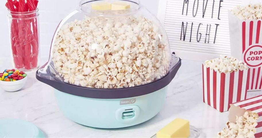 dash popcorn maker sitting on counter with popcorn bags and butter sitting around it