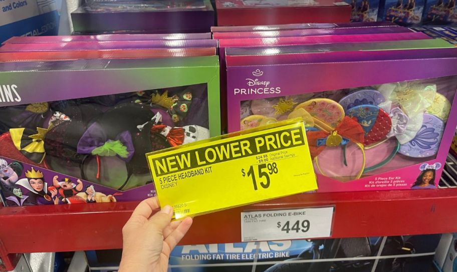 womans hand holding a yellow pricing sign in front of two sets of disney mouse ears