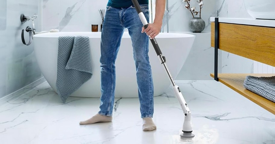 man using electric spin brush cleaning floor in bathroom 