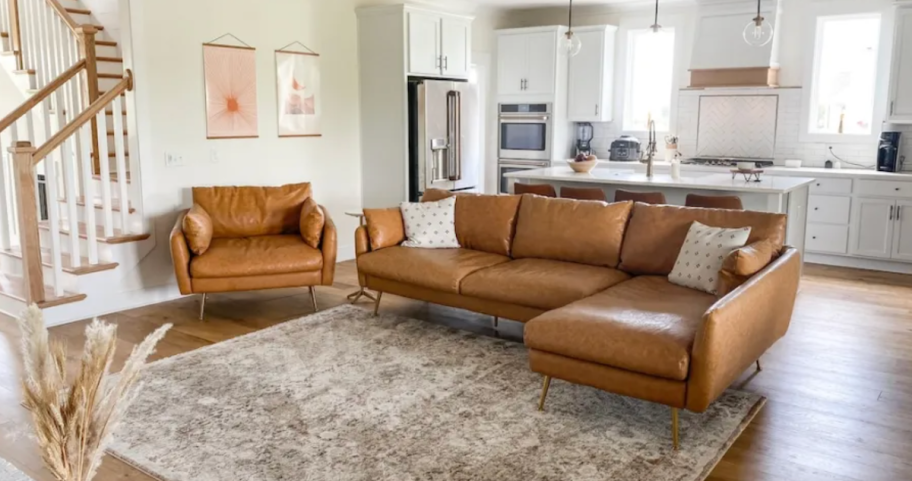 faux leather couch and chair in living room with rug and open white kitchen 