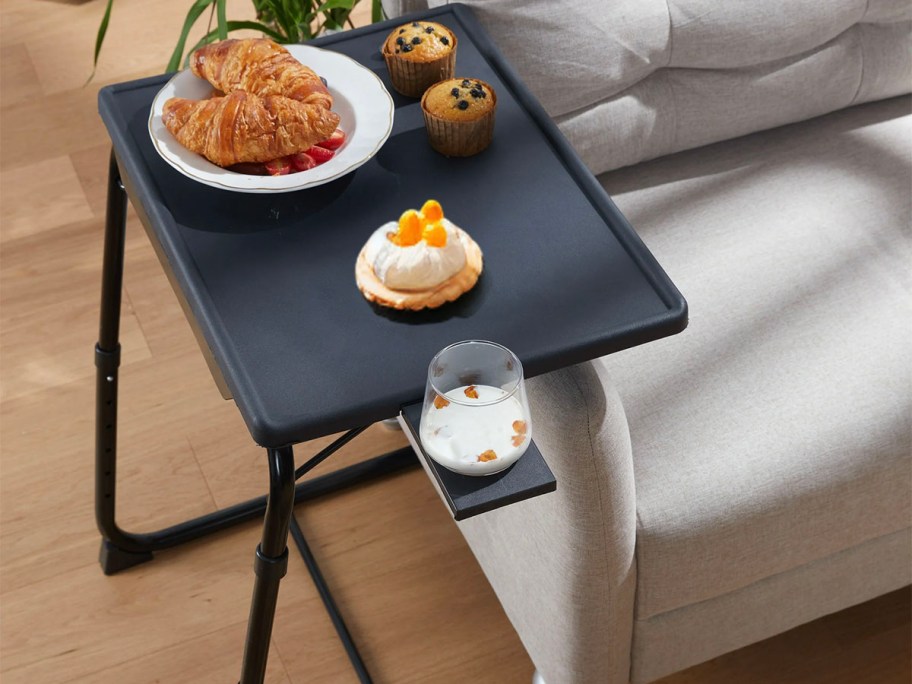black folding tray table with food and drink on top next to couch