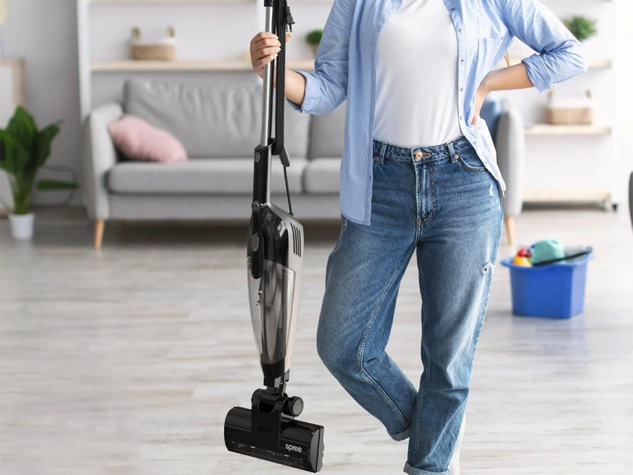 woman holding black stick vacuum in living room 