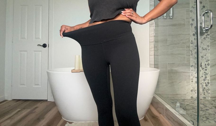 woman holding out side of black leggings standing in bathroom
