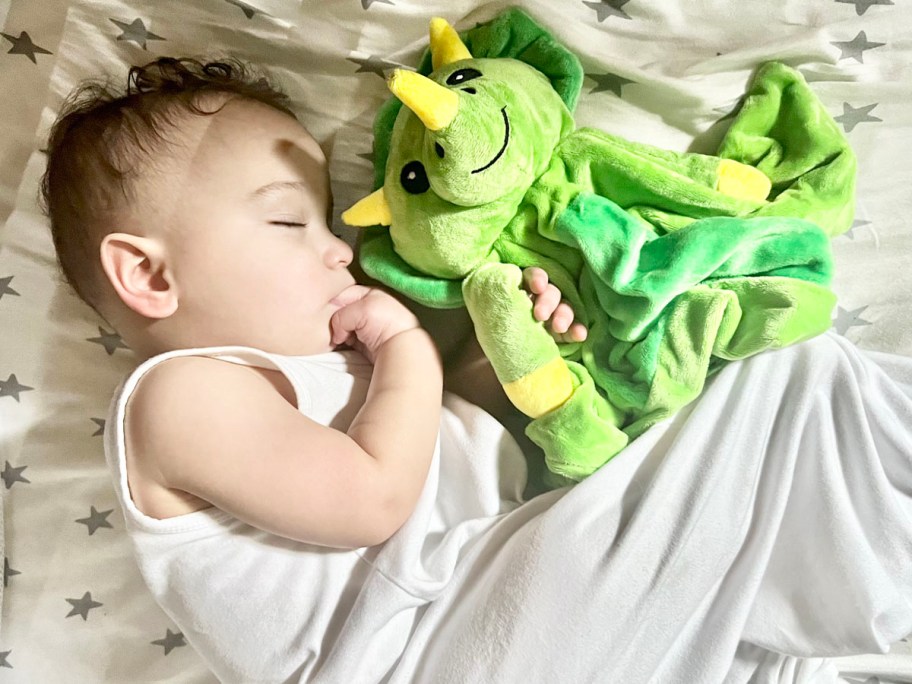 little boy sleeping with green dragon plush in crib