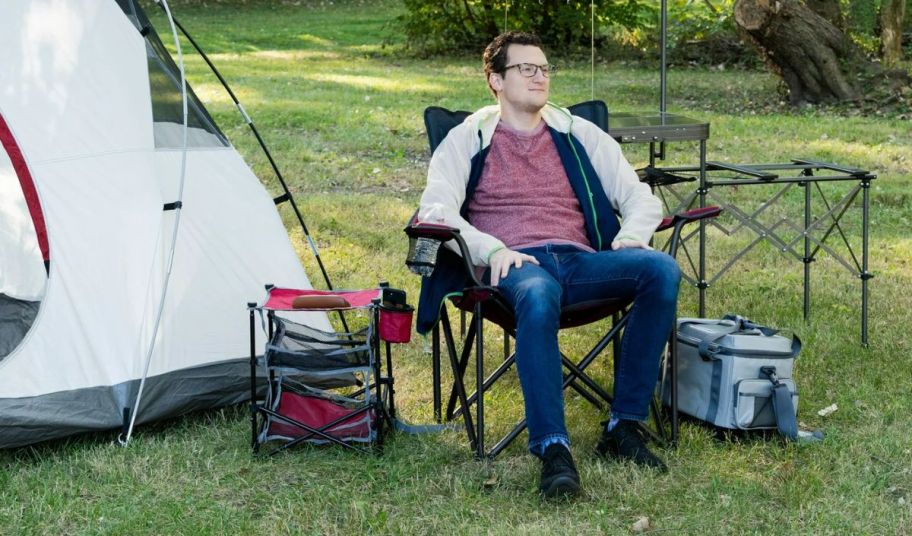 man sitting at a camp site in a red ozark trail camp chair