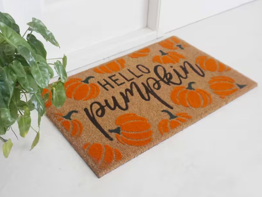 white front door with brown coir doormat with orange pumpkins that says "Hello there pumpkin"