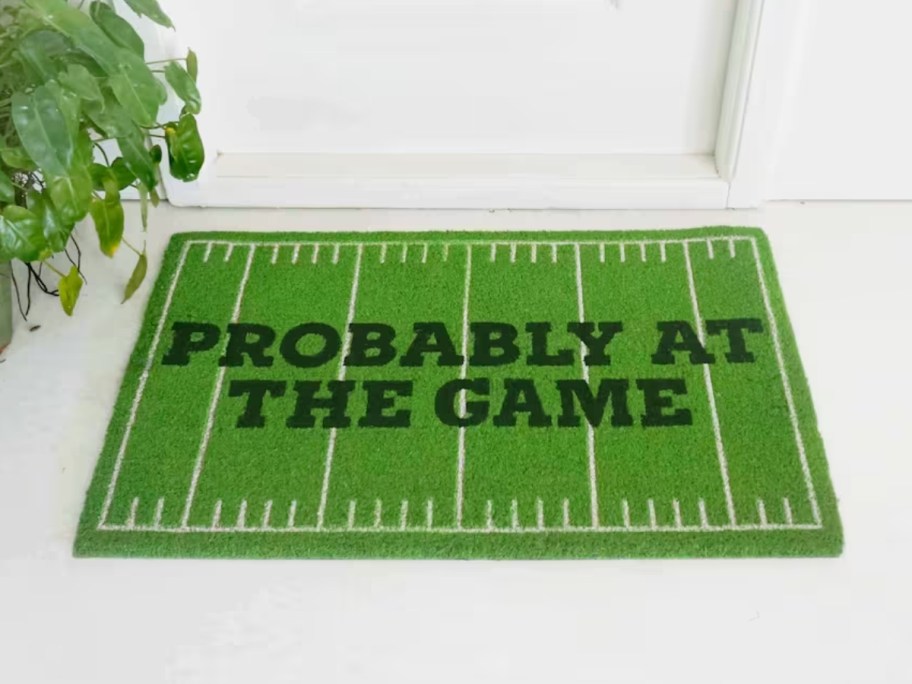 doormat with a green football field that says "probably at the game" in front of a white door