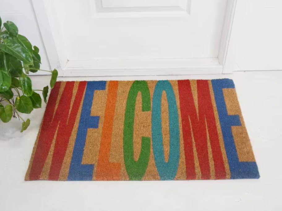 a coir doormat with the word "welcome" in colorful letters in front of a door