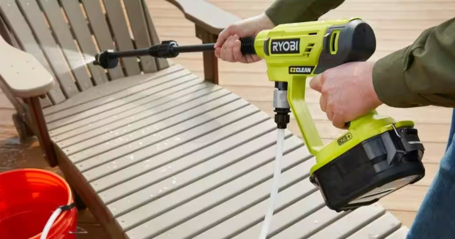 person using a yellow Ryobi pressure washer to clean a deck chair