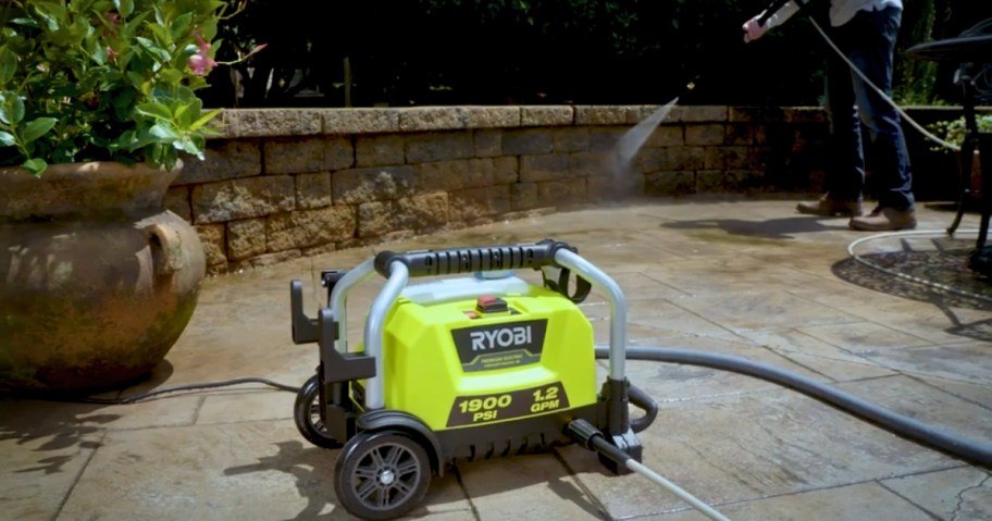 yellow Ryobi corded large pressure washer with person behind it pressure washing a patio area