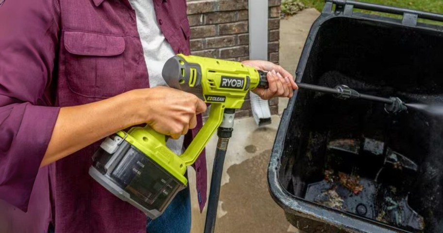 woman using a yellow Ryobi pressure washer to clean out a trash can outdoors