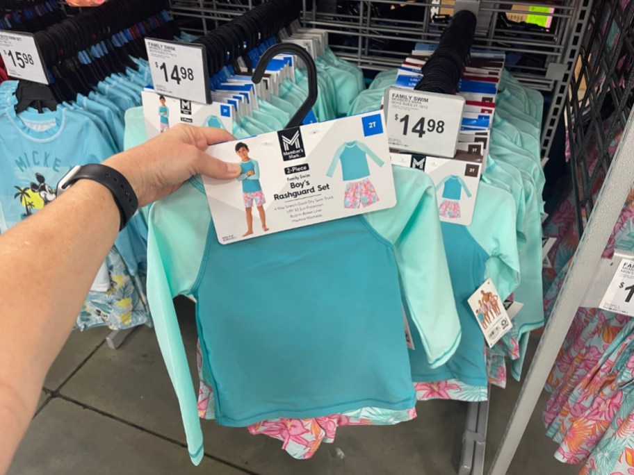hand holding a boy's 2 pc bright, tropical floral swimsuit set at Sam's Club