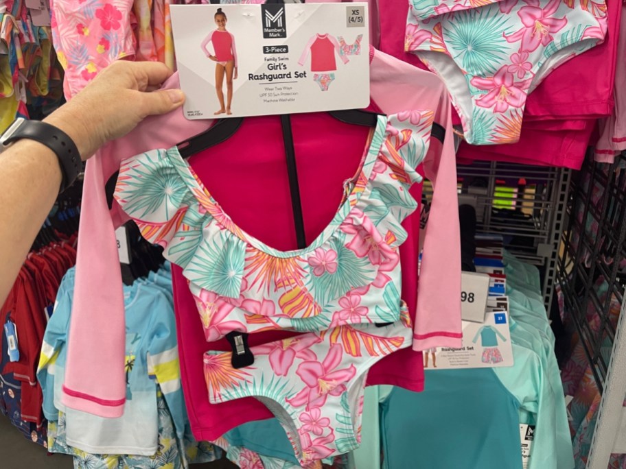 hand holding a girl's 3 pc bright, tropical floral swimsuit set at Sam's Club