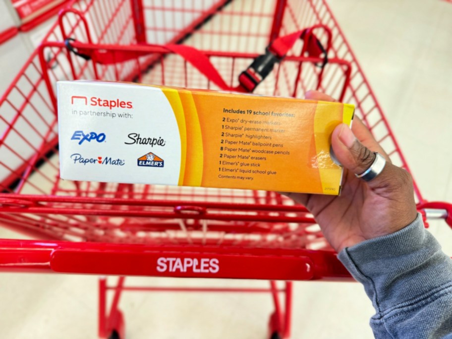 staples teacher supply kit in hand over a red shopping cart