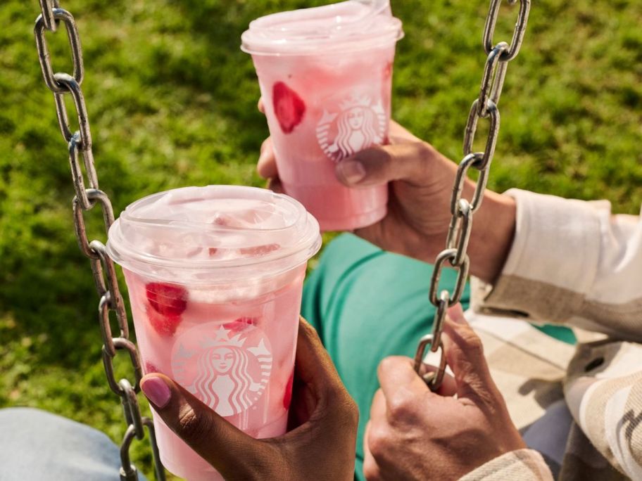 two starbucks drinks being held by hand by two people on swings